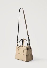 Μπεζ ορθογώνια τσάντα με μαύρο περίγραμμα, δύο κοντά χερούλια και μακρύ ρυθμιζόμενο ιμάντα ώμου σε λευκό φόντο.