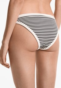Närbild av en person som bär svartvita randiga bikiniunderbyxor, som visar nedre delen av ryggen och övre delen av låret.