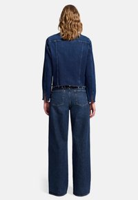 Jeansjacke und weit geschnittene Jeans in Dunkelblau. Die Jacke hat ein kurzes Design mit rohen Kanten; die Jeans verfügen über zwei Gesäßtaschen und einen lockeren Schnitt.