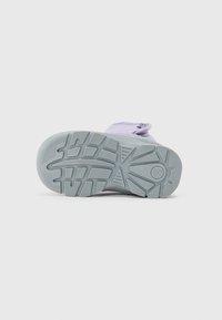 Calzado de color púrpura claro con una suela de goma texturizada. Presenta una punta redondeada y una suela gris claro en contraste, con un diseño de tracción estampado.