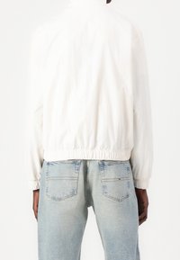 White, lightweight bomber jacket with a round neck and elastic cuffs, paired with light blue denim jeans featuring back pockets.