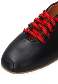 Černá kožená bota s kulatou špičkou, s výřezem a živými červenými šněrovadly. Podešev je v tan barvě, což zdůrazňuje štíhlý design boty.