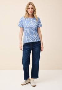 Ljusblå t-shirt med vitt bladmönster, kombinerat med mörkblå vida jeans och vita sneakers. Enkel, avslappnad outfitdesign.