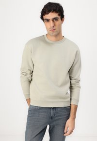 Maglione girocollo grigio chiaro realizzato in un tessuto morbido, con polsini e orlo a costine, dotato di un piccolo logo sul petto.