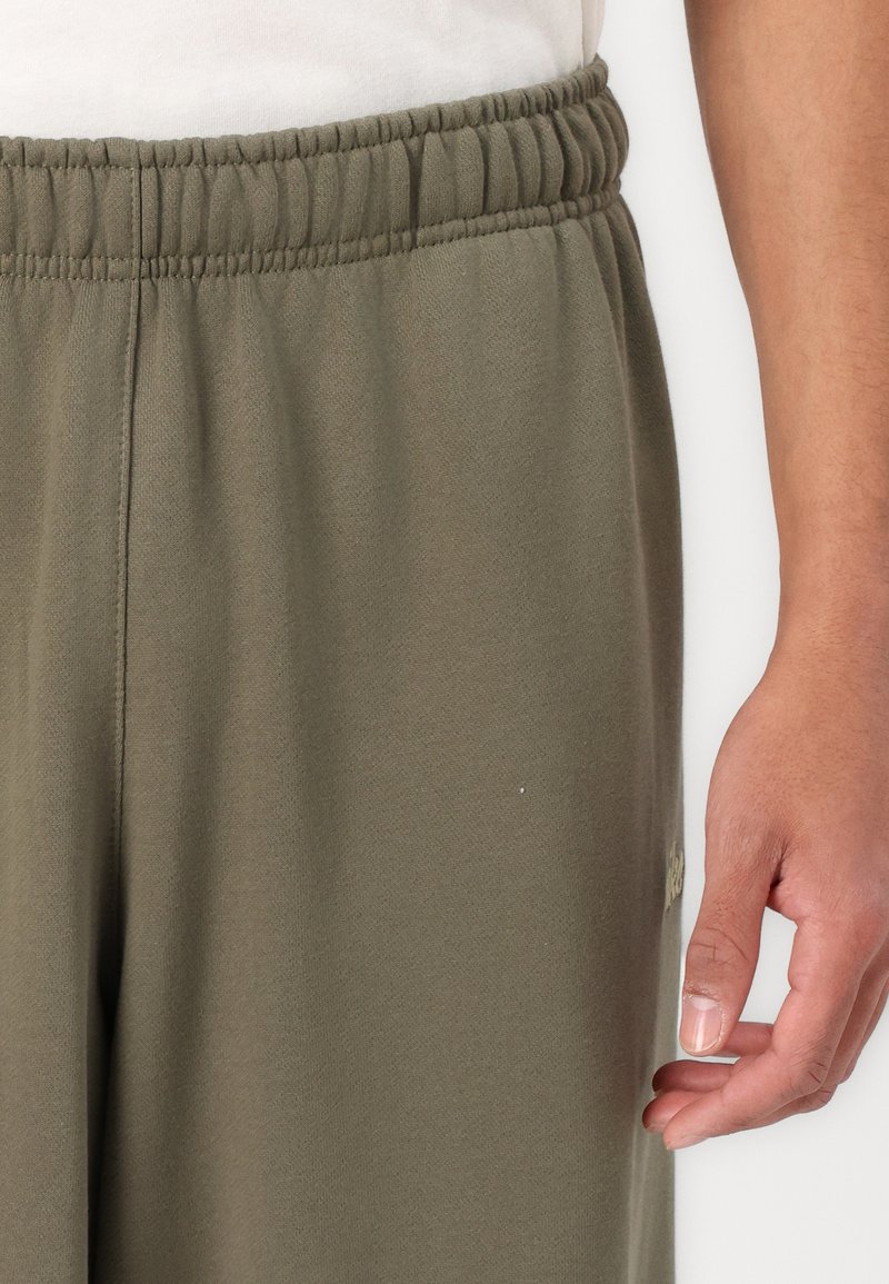 Oliwkowe dresy z elastycznym pasem i bocznymi kieszeniami na ręce, wykonane z miękkiego materiału, z subtelnym logo na udzie.