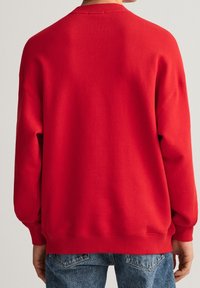 Sudadera roja con cuello redondo, puños y dobladillo acanalados, y corte relajado. Tejido de algodón, diseño simple y sin patrones ni logotipos visibles.