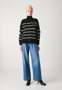 Black and white striped knit sweater with high collar, paired with wide-leg light blue denim jeans and black ankle boots.