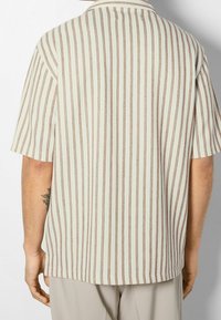 Koszula z krótkim rękawem w jasnym kremowym kolorze z pionowymi brązowymi paskami, z klasycznym kołnierzykiem i luźnym krojem. Tkany materiał z bocznymi rozcięciami.