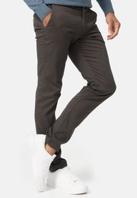 Pantalons slim gris foncé en tissu lisse, avec des poches avant et assortis à des baskets blanches. Design ajusté avec une silhouette moderne.