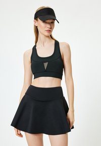 Svart atletisk outfit med en åtsittande sport-bh med nätdetaljer och en urtillverkad skort. Materialet ser slätt och stretchigt ut.