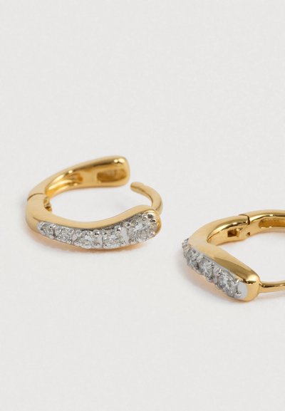 Cercei creole din aur cu un design curbat, având un rând de pietre clare și strălucitoare așezate de-a lungul unei părți. Textură metalică netedă.