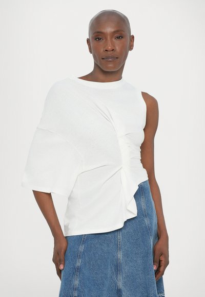 Biely asymetrický top s krátkymi rukávmi, s prehnutým detailom vpredu, kombinovaný s džínsovou sukňou. Hladká textúra, moderný dizajn.