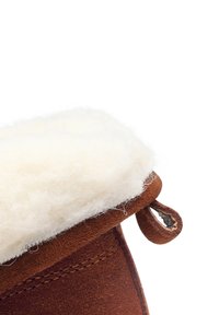 Rudas zomšinis batas su kreminės spalvos tekstūruota kailio pamušalu. Pats batų dizainas turi mažą kilpą, kad būtų lengva užsiauti, pabrėžiant rankų darbo meistriškumą ir kokybę.