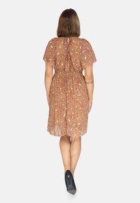 Vestido floral marrón con mangas cortas, cintura ceñida y falda ligeramente acampanada. La tela es ligera y tiene un patrón texturizado.