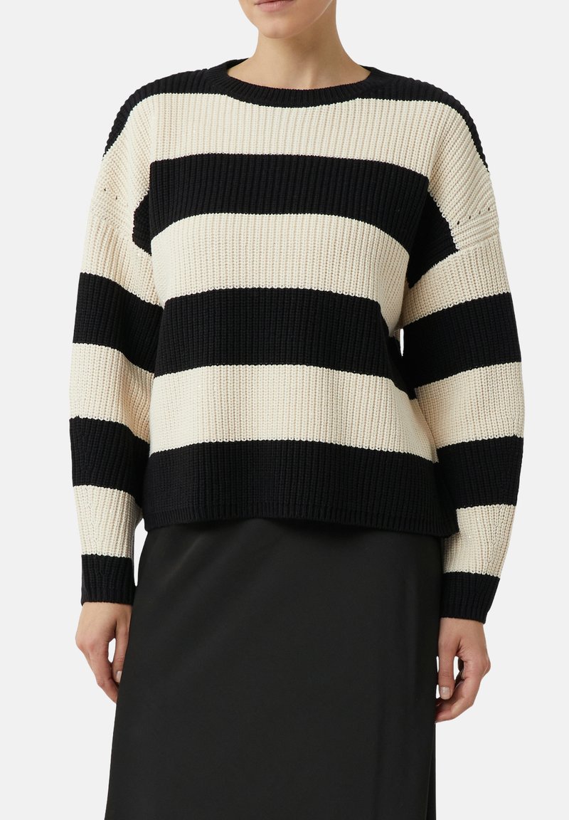 Woman wearing a black and white wide horizontal striped knitted sweater with long sleeves and a black skirt.