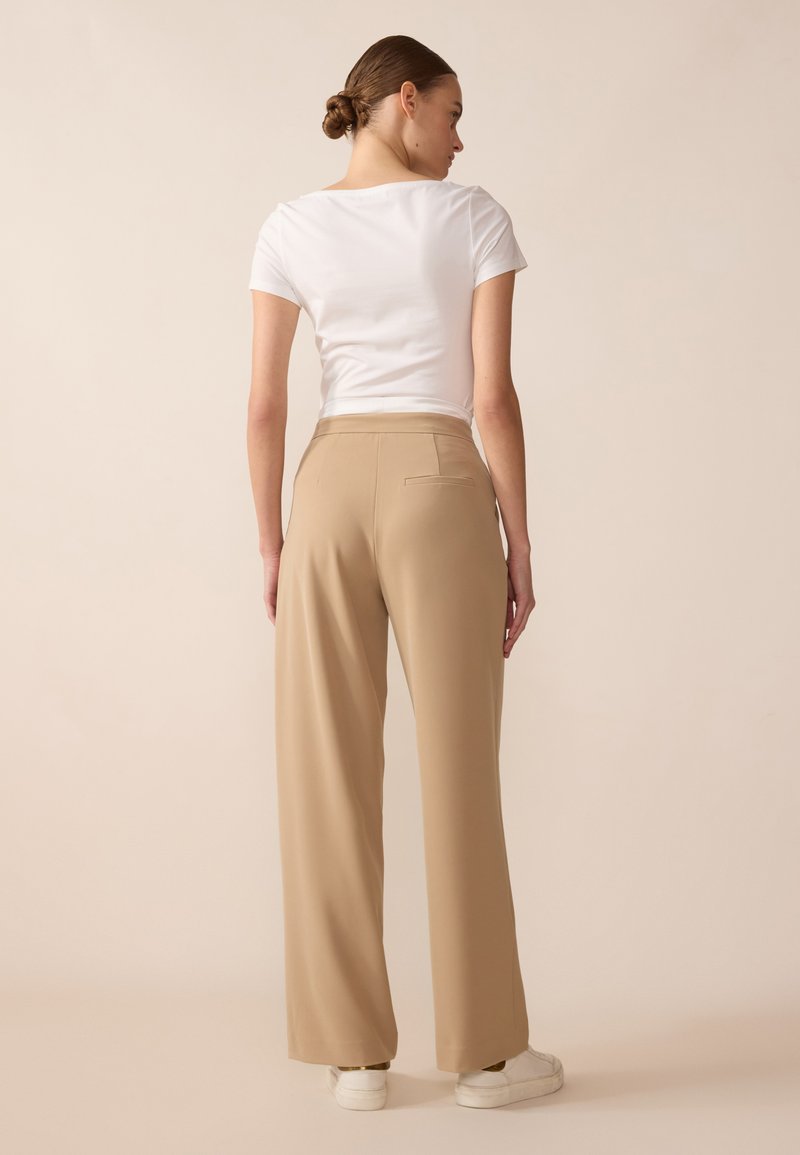 T-shirt bianco a maniche corte abbinato a pantaloni beige a vita alta e gamba larga e sneakers bianchi. Il tessuto è liscio con una leggera lucentezza.