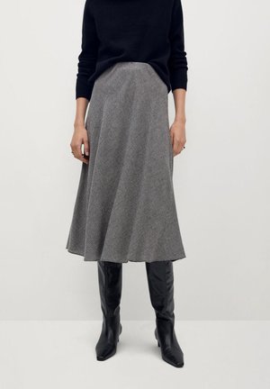 Person wearing a black long-sleeve top, gray patterned midi skirt, and black knee-high leather boots, standing against a plain light background.