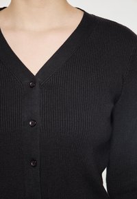 Černý žebrovaný kardigan s hlubokým V-výstřihem, zapínáním na knoflíky a dlouhými rukávy, vyrobený z měkké, texturované tkaniny.