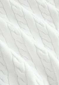 Dús, fehér kötött anyag, amely kábelmintával és kiemelkedő textúrával rendelkezik. Puha és sima felület, jól látható öltés részletekkel.