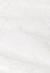 Tissu avec un motif floral blanc, possédant une surface texturée, avec des motifs en relief et une apparence lisse et douce.