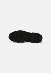 Black rubber shoe sole with horizontal grooves, round toe, textured grip patterns, and molded features for traction and support.