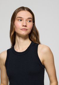 Marinblå ärmlös stickad topp med rund halsringning, ribbade kanter och figurnära silhuett. Mjuk struktur och jämn färgfördelning.