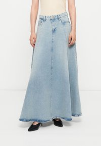 Lyseblå denimskjørt med en flagrende design, har råkant, fem lommer og knappestolpelukking. Kombinert med svarte hælsko.