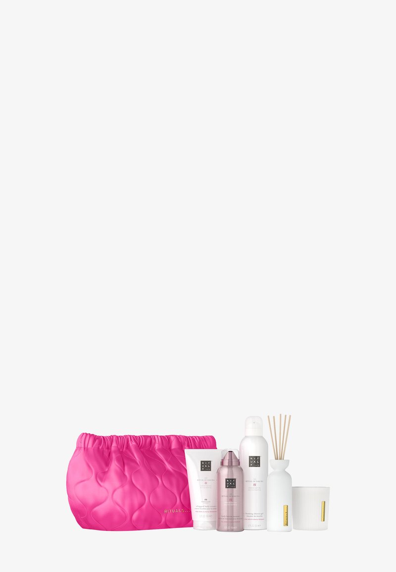 Rosa quiltet kosmetikkmapp med flere hvite og rosa hudpleieprodukter, en reed diffuser, og et teksturert hvitt lys.