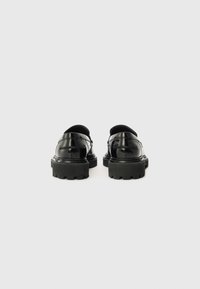 Des chaussures en cuir noir avec une finition brillante, dotées d'une semelle noire épaisse, d'un bout arrondi et d'un design minimaliste, vues de l'arrière.