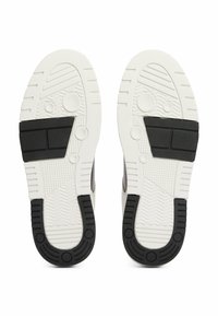 Schoenenzolen met zwarte rubberaccenten, witte gestructureerde buitenzool, voorzien van groeven en cirkelpatronen voor grip en duurzaamheid.