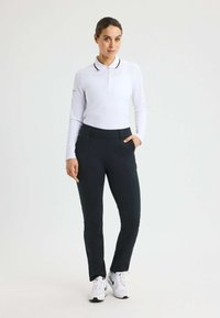Wit poloshirt met lange mouwen, een zwarte kraag en knoopdetails, gecombineerd met zwarte kledingpantalons en witte sportschoenen.