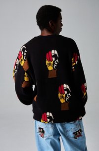 Suéter negro de punto con motivos gráficos coloridos de manos y diseños abstractos. Combinado con jeans azul claro adornados con detalles bordados.