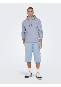 Sudadera con capucha de color gris claro con un bolsillo frontal, combinada con shorts de mezclilla azul claro. Completada con zapatillas negras y blancas.