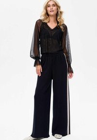 Czarna, przezroczysta bluzka z koronkowym wykończeniem, zestawiona z czarnymi spodniami o szerokich nogawkach z paskiem po boku i teksturowanym detalem.