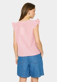 Blusa a righe rosse e bianche con maniche corte a volant, realizzata in tessuto leggero, abbinata a pantaloni corti in denim blu.