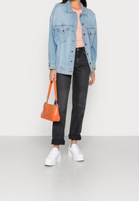 Ljusblå denimjacka, skjorta med orange ränder, svarta uppvikta jeans, vita plattformssneakers, orange handväska med kedjedetalj.