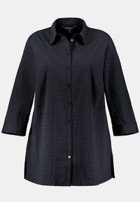 Camicia nera con bottone, realizzata in tessuto testurizzato, con colletto, maniche lunghe e spacchi laterali per facilitare i movimenti.