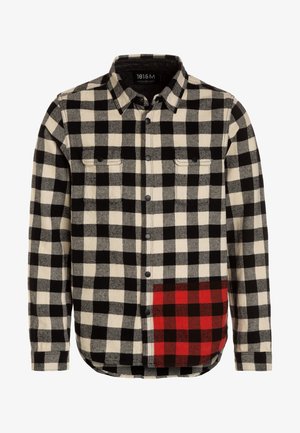Langärmliges Hemd mit Knopfleiste mit schwarz-weiß kariertem Muster und einem rot-schwarz karierten Patch an der unteren rechten Seite.