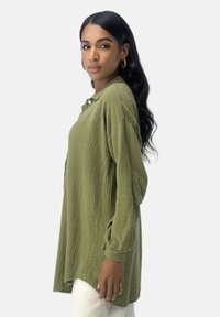 Langsleeveshirt in olijfgroen gekreukt materiaal met een knoopkraag en een ontspannen pasvorm, met manchetten en zijsplitten voor meer bewegingsvrijheid.