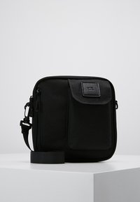 Sort nylon crossbody taske med en struktureret overflade, lynlås lukning, frontlomme med klap, justerbar rem og mærke på fronten.