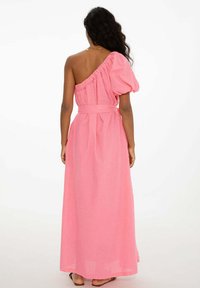 Asymetrické šaty na jedno rameno v žiarivej ružovej farbe s naškrobeným pufovaným rukávom, opásaným pásom a splývavou, dlhou sukňou. Ľahký materiál.