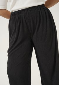 Schwarze, plissierte Hose mit einem elastischen Bund, aus einem strukturierten Stoff und mit einem lockeren Schnitt, geeignet für Freizeitkleidung.