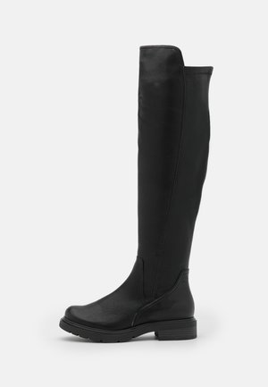 Botte haute en cuir noir avec bout rond, talon bas et épais, finition lisse, debout sur un fond blanc uni.