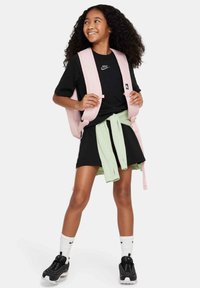 T-shirt nera, felpa verde menta legata in vita, gonna nera, zaino rosa, calze bianche con logo nero, sneakers nere con ammortizzazione.