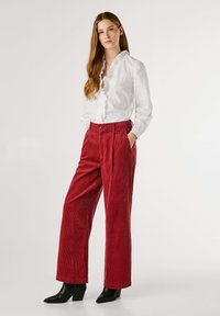 Blusa bianca con volants e pantaloni a palazzo in velluto a coste rossi con tasche laterali. Stivaletti neri con tacco completano l'outfit.
