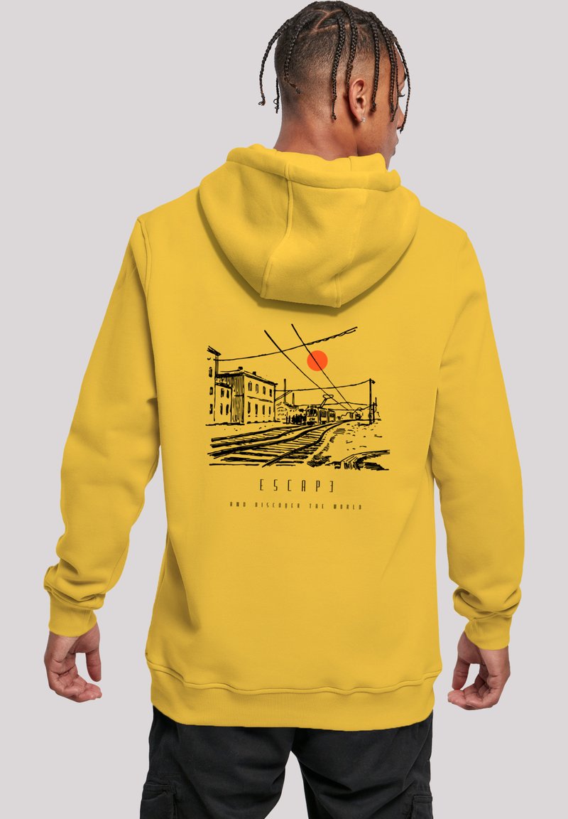 Yellow hoodie featuring a black graphic of a linear landscape with buildings and a sun. Text below reads "ESCAPE AND DISCOVER THE WORLD."