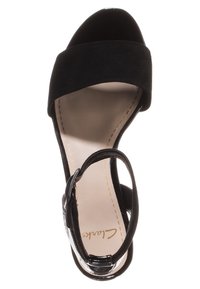 Sandale en suede noire avec un capuchon de orteil noir brillant, une large bride à l'avant, une fermeture à boucle autour de la cheville, et une semelle intérieure lisse beige.