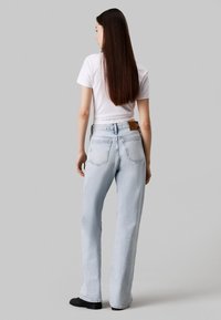 Jeans de mezclilla de color azul claro con un ajuste relajado, que cuentan con un diseño clásico de cinco bolsillos y una parche de cuero marrón en la parte trasera de la cinturilla.
