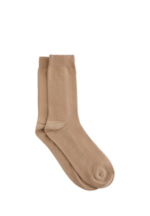 Chaussettes beiges avec un motif en maille texturée et des poignets côtelés. Le matériau semble doux et élastique, fini par un bout arrondi.