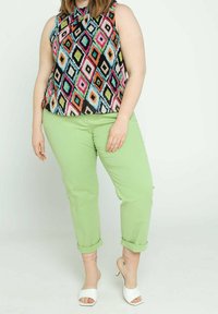 Ärmlös topp med ett mångfärgat diamantmönster på svart bakgrund, i kombination med ljusgröna byxor med uppvikta ärmar och vita klacksandaler.